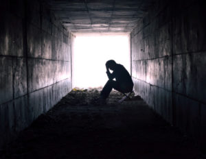 This is a black and white picture of a person sitting at the end of a dark tunnel with a bright white light at the end. It is used because of its ability to demonstrates how mental illness such depression, anxiety, and PTSD can keep us stuck in a dark place and that only we can move closer towards healing ourselves.